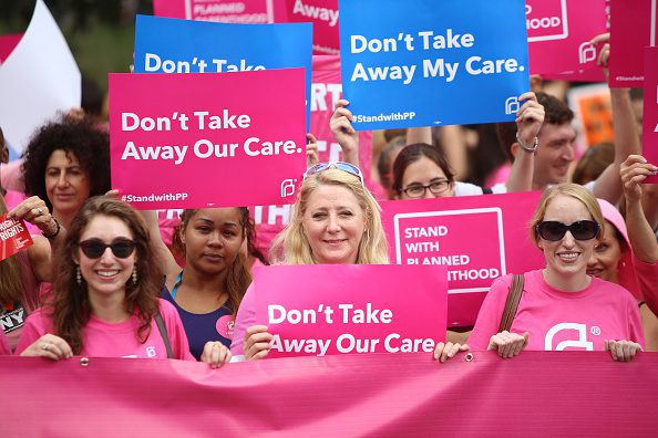 Participants hold pink Planned Parenthood banner and signs.